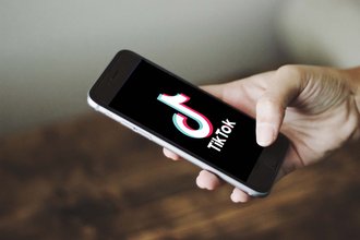 A hand holds a phone displaying the TikTok icon and the words "TikTok"