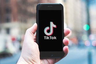 A hand holds up a phone with a black screen and the words "TikTok" below the app's logo.