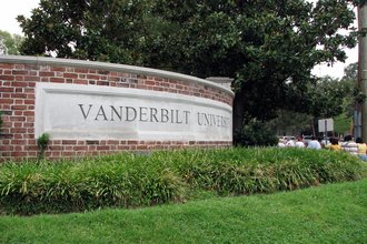 A curved brick wall with the words "Vanderbilt University" stands behind grass and bushes, with a large tree in the background