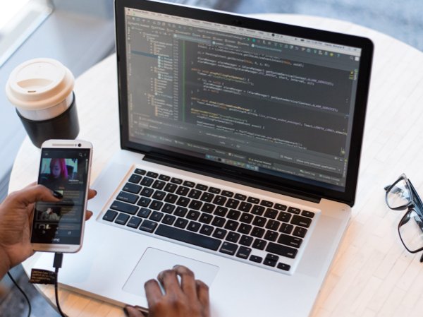 Header image of a woman coding and using her phone at a desk