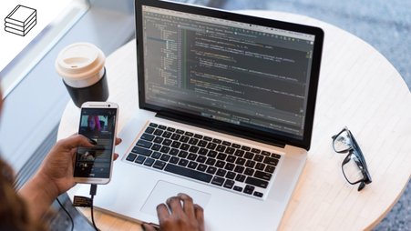 Header image of a woman coding and using her phone at a desk
