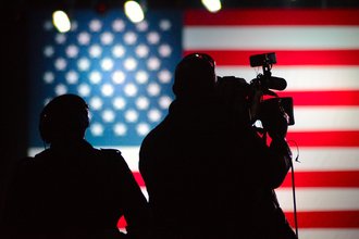 a cameraperson filming in front of an American flag