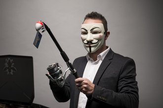 Photo of a man in a Guy Fawkes mask, with a fishing reel in hand.