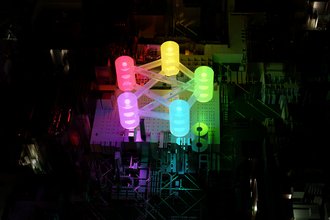 Digital art showing lights lit up in different colors, connecting with each other by beams, in a dark room.