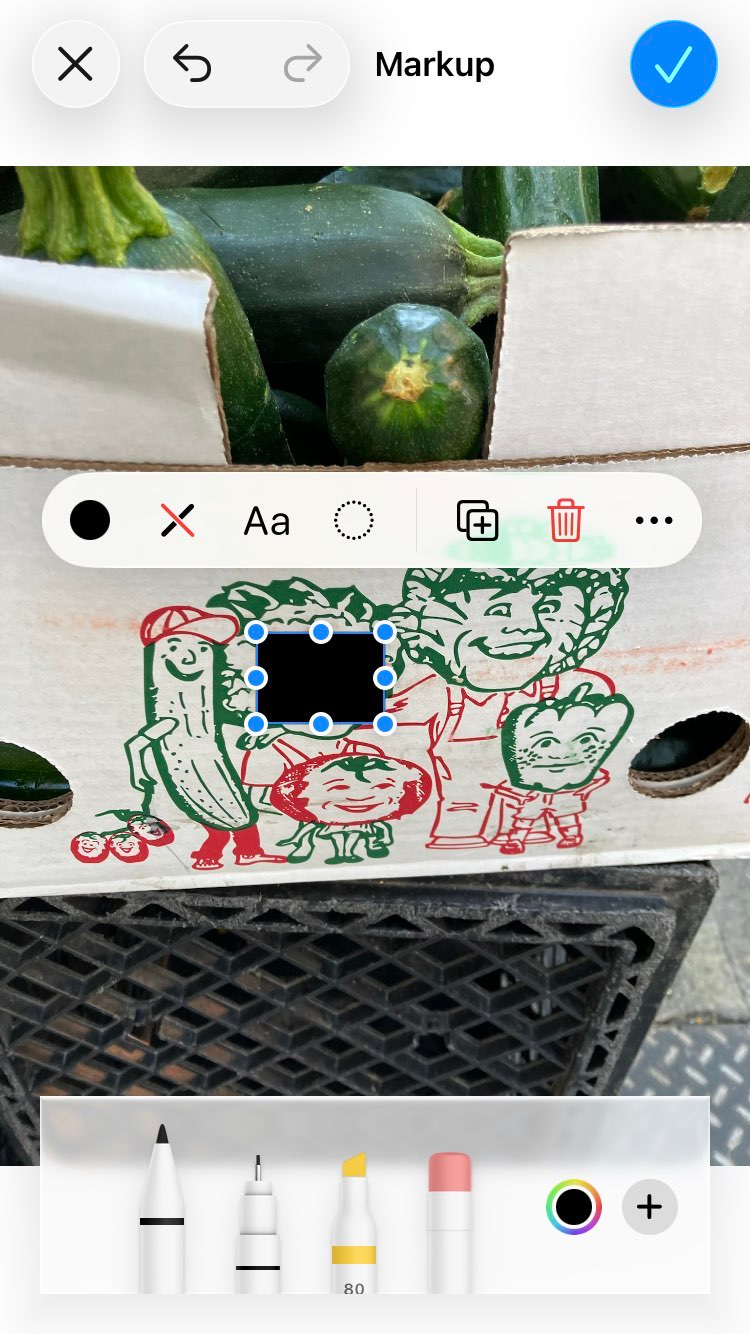 A screenshot of iOS's Photos app showing a black rectangle drawn over a face in an illustration of anthropomorphized vegetables on the side of a produce box.