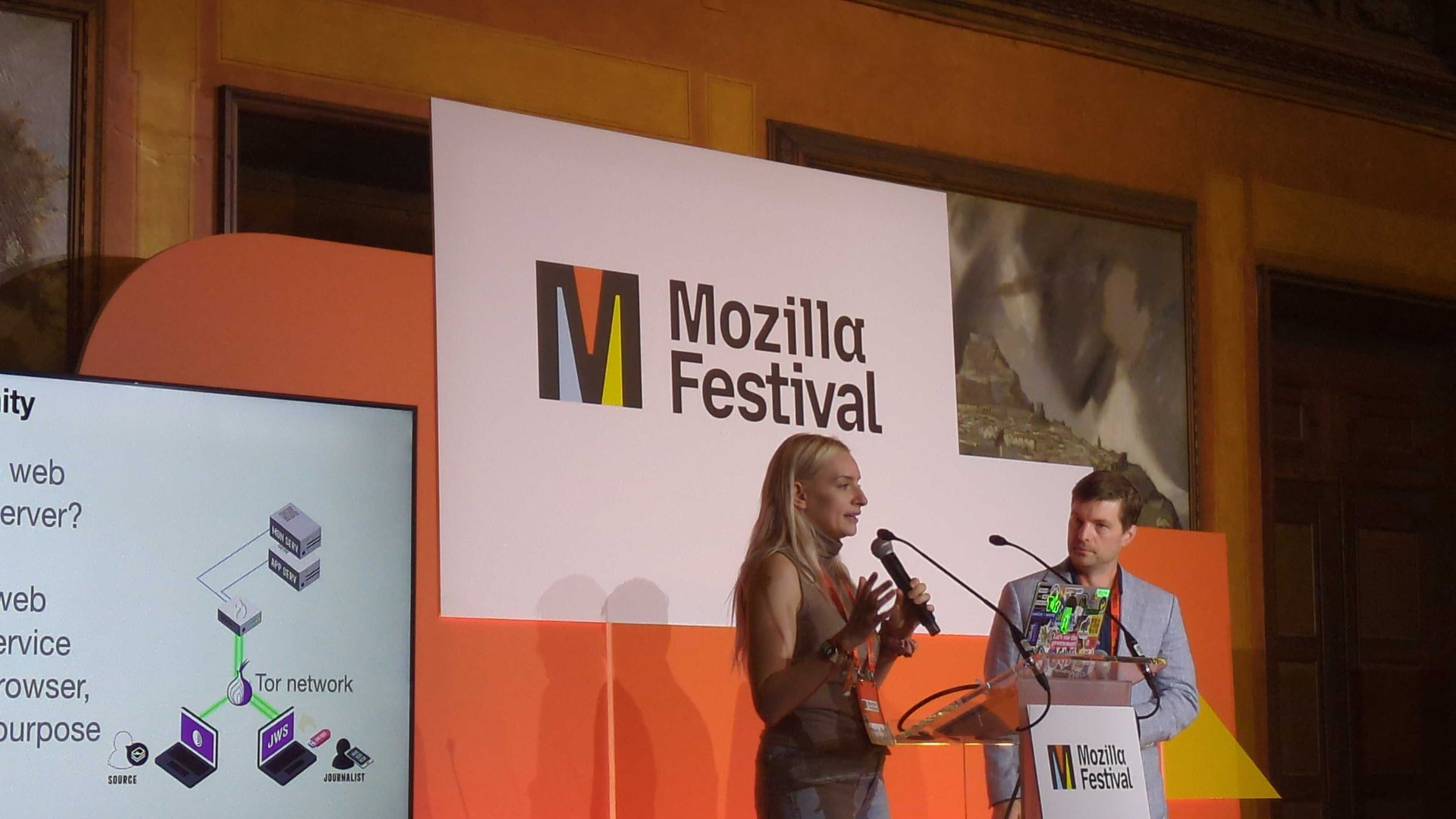 Freedom of the Press Foundation’s Jennifer Helsby, standing at a podium next to FPF’s Trevor Timm on a stage at the November 2025 Mozilla Festival in Barcelona, Spain.