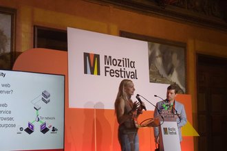 Freedom of the Press Foundation’s Jennifer Helsby, standing at a podium next to FPF’s Trevor Timm on a stage at the November 2025 Mozilla Festival in Barcelona, Spain.