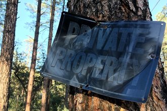 A header image of a metal sign mounted on a tree in a forest reading, "private property."