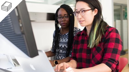 Two women in front of their computers, sharing a desk.