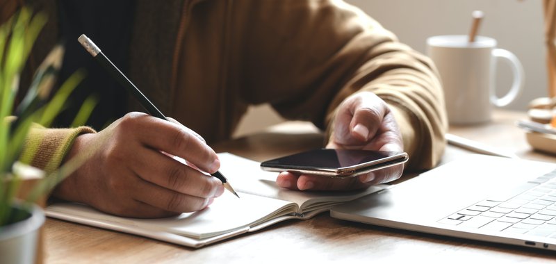 Cover image of a person holding a smartphone while writing