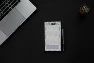 Photo of a desk with a "to do list" notepad, a computer, and a small cactus.