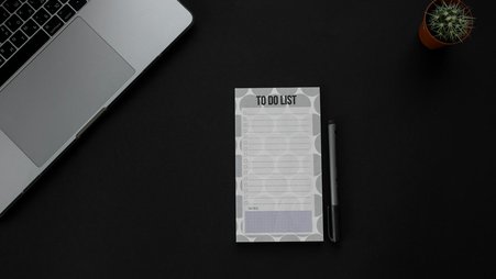 Photo of a desk with a "to do list" notepad, a computer, and a small cactus.